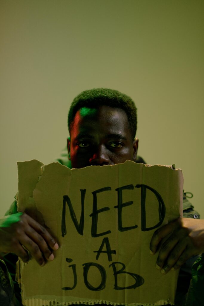 A man holding a cardboard sign reading 'Need a Job', highlighting unemployment and social issues.